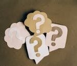 Four paper cutouts of question marks in beige and white on a brown surface, symbolizing inquiry and curiosity.
